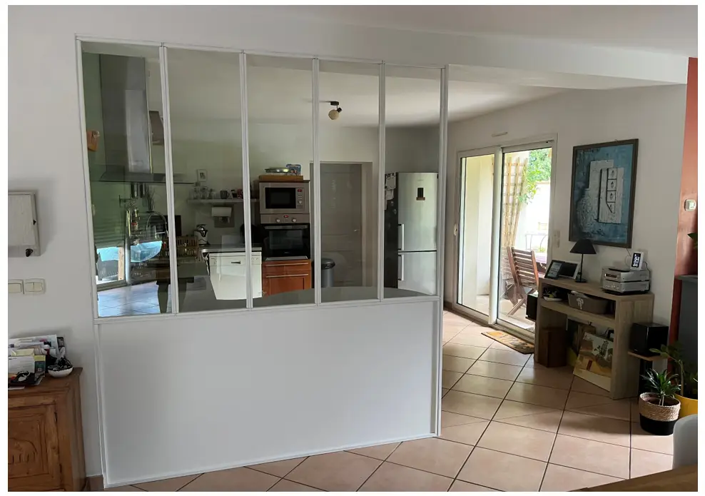 Glass-walled kitchen partition with white frame separating a modern kitchen from the living area, seen from the dining room hall.