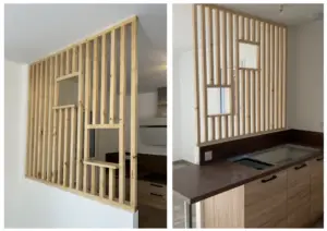 Wooden vertical slat room divider with built-in shelves separating a kitchen and living area in a modern interior.