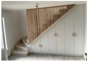 Modern staircase with vertical wooden slats railing, and white built‑in cabinets beneath along a light gray floor.