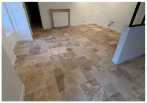 Room with unfinished tile floor in neutral beige tones; empty walls, frame leaning against back wall, and exposed outlets suggesting renovation.